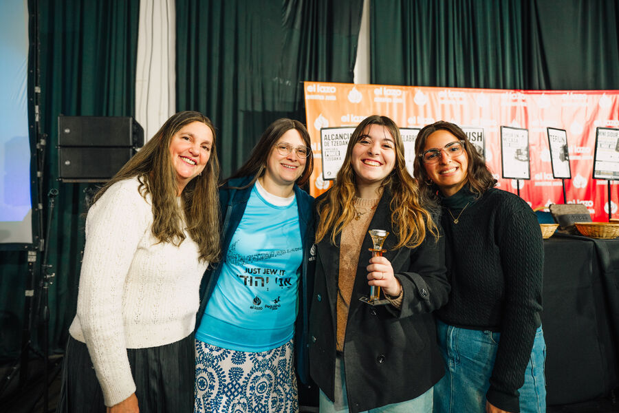 Chicas sonriendo junto a carteles de la campaña de tzedaká